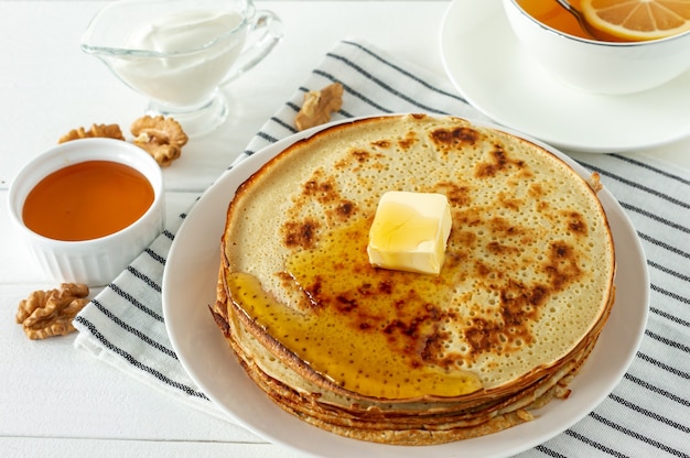 Pancakes served with honey syrup and butter on a white plate. Traditional crepes for pancake week or Shrovetide.