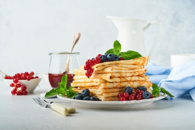 Pancakes stack of crepes or thin pancakes with berries\
blueberries red currants raspberries and honey for breakfast\
homemade breakfast copy space selective focus