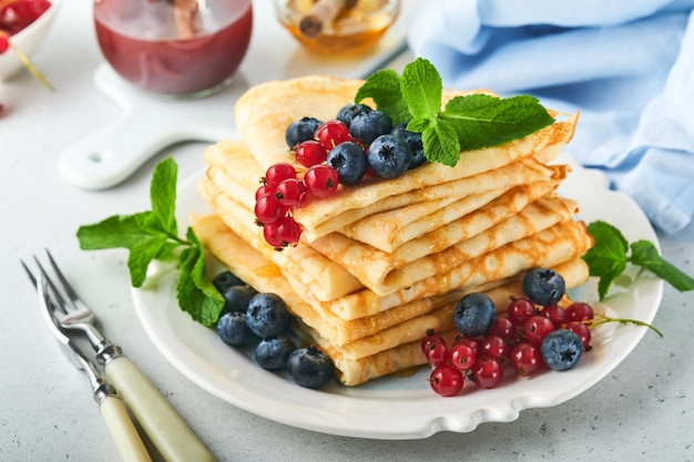 Pancakes Stack of crepes or thin pancakes with berries blueberries red currants raspberries and honey for breakfast Homemade breakfast Copy space Selective focus