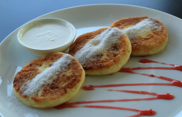 Pancakes syrniki sprinkled with caster sugar served with sour cream and jam