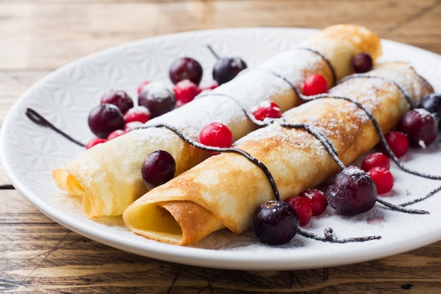 Pancakes tube with chocolate and berries on a plate. Wooden background.