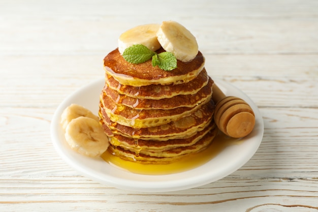 Pancakes with banana and honey on white wooden table