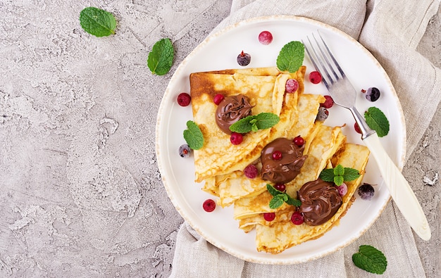 Pancakes with berries and chocolate decorated with mint leaf. Tasty breakfast. Top view