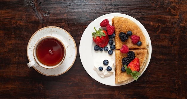Pancakes with berries and sour cream on a dark wooden background