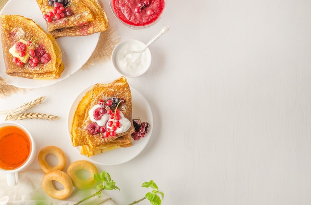 Photo pancakes with berries, sour cream and tea for the russian holiday maslenitsa on a white plate with copy space