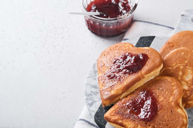 Frittelle con marmellata di frutti di bosco e miele a forma di cuore e tazza di caffè calda su sfondo bianco di legno concetto colazione per san valentino o piacevole sorpresa per la persona amata tavolo visto dall'alto