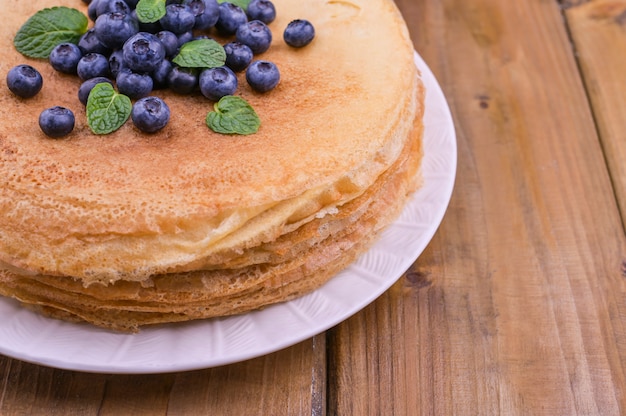 写真 木製の屋根の上の皿にブルーベリーと蜂蜜のパンケーキ。マスレニツァのロシアのお祭りのための伝統的なペストリー。テキスト用の空き容量。