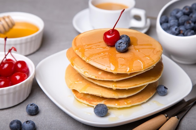 Pancakes with blueberries cherries and honey Closeup Selective focus