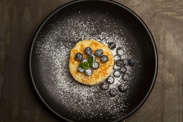 Pancakes with blueberries and icing sugar on a black plate in a top view