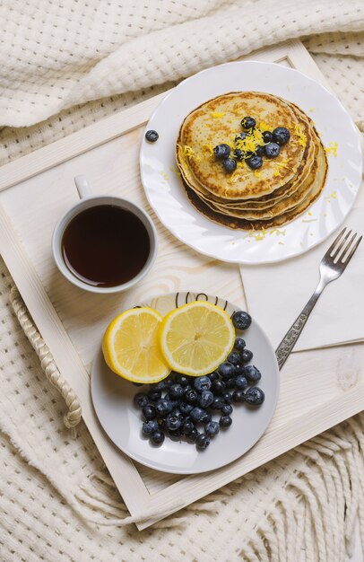 Pancakes with blueberry and cap of coffee on a wooden tray on a bed.