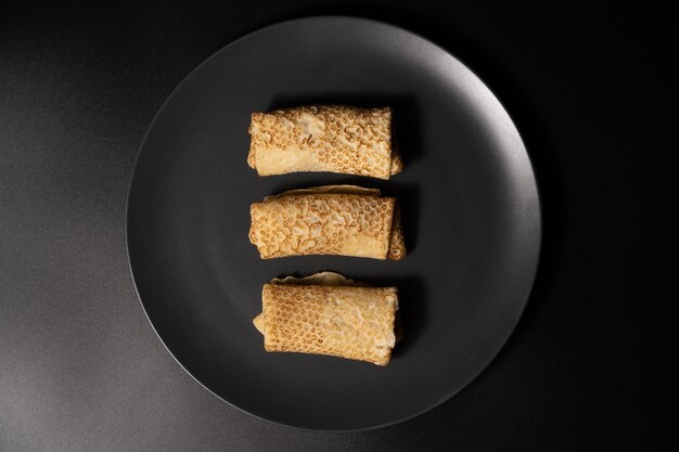 Pancakes with cheese on a plate and kitchen utensils on a black background