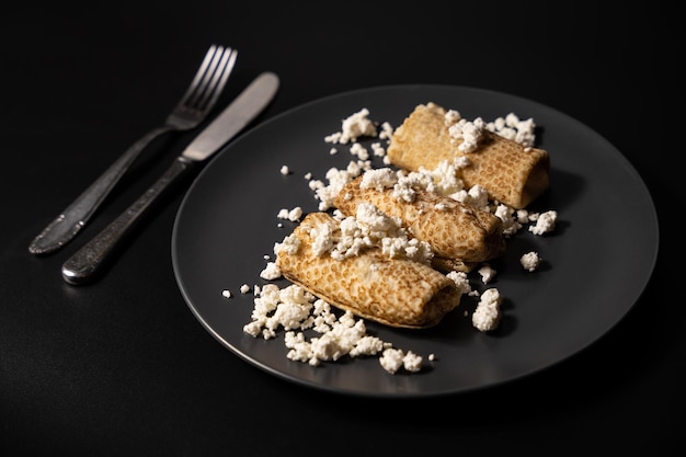 Pancakes with cheese on a plate and kitchen utensils on a black background