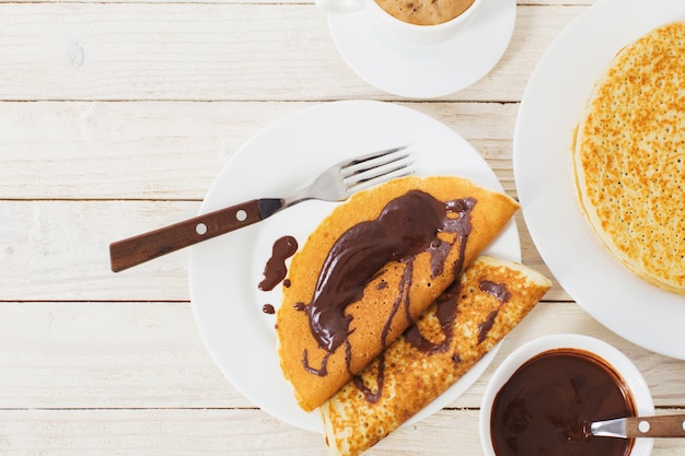 Pancakes with chocolate and coffee on white wooden table