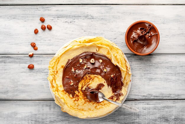 Pancakes with chocolate paste and hazelnuts, on a white plate on wood