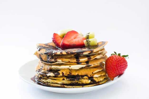 Pancakes with chocolate, strawberries and kiwi on white background