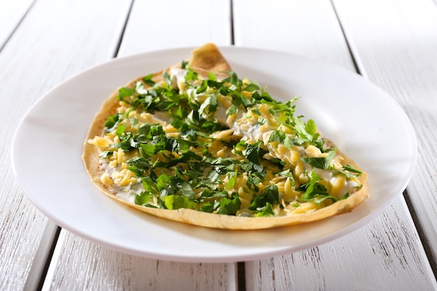 Pancakes with cream cheese and greens in plate on wooden table closeup