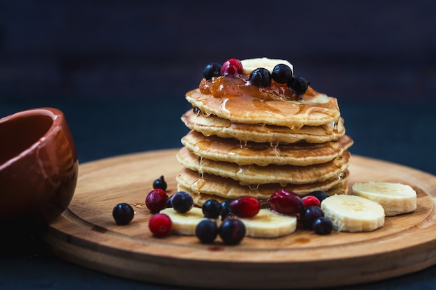 Pancakes con miele, banane, marmellata e bacche su un piatto di legno menu, ricetta del ristorante. servito in