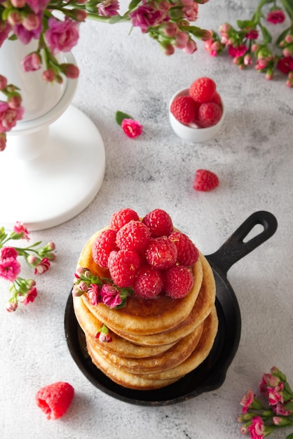 Pancakes with honey decorated with raspberries and flowers top\
view