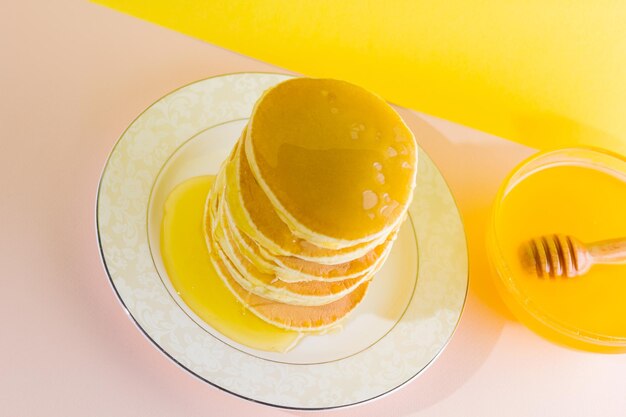 Pancakes with honey on yellow pink background Pancakes on white plate and honey Delicious dish for breakfast Close up