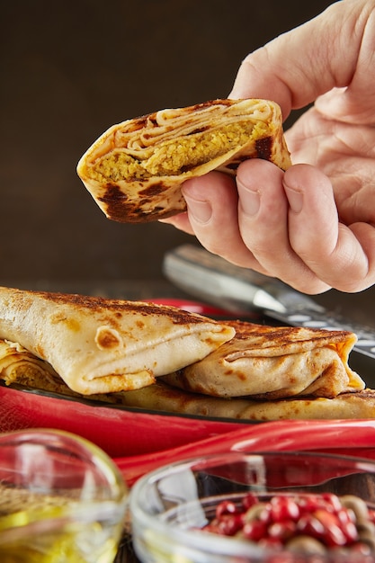 Pancakes with meat, holds by hand, with oil and tongs on plate on dark wooden background.