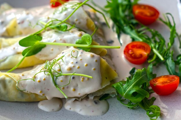 Pancakes with mushrooms in a sauce decorated with greens and tomatoes