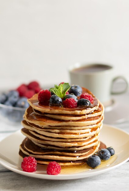 Pancakes with raspberries blueberries and tea on a light background closeup