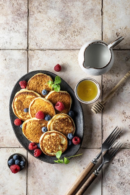 Pancakes with raspberry and blueberry mint leave honey and rustic cutlery on pink tile background top view