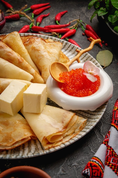 Photo pancakes with red caviar and butter on a gray plate and with a wooden spoon maslenitsa