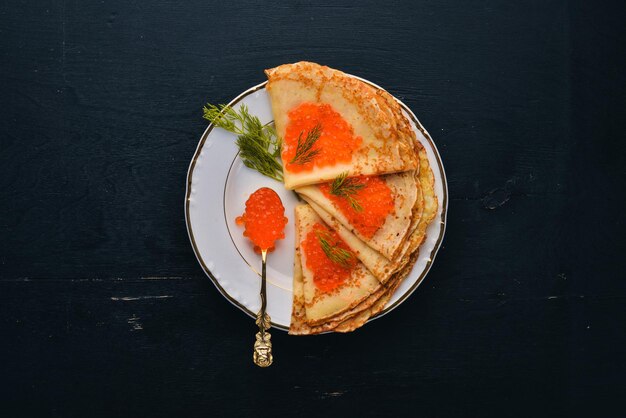 Pancakes with red caviar on a plate On a wooden background Top view Free space for text