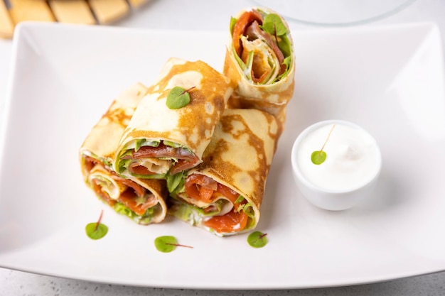 Pancakes with salmon trout sour cream and greenstuff Thin not sweet blinchiki stuffed with red fish Traditional Russian and Ukrainian dish Feast of Maslenitsa Selective focus closeup