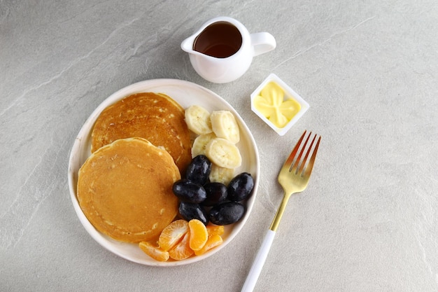 Pancakes with slices of fresh bananas orange and grapes fruit