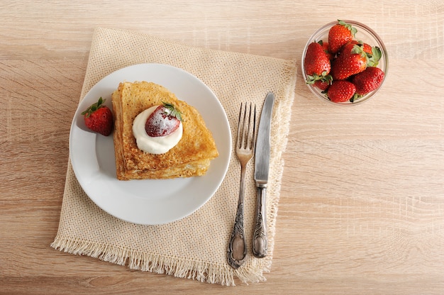 Pancakes with sour cream and strawberries in a plate