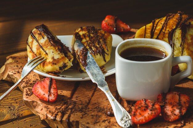 Pancakes with strawberries chocolate and coffee on a wooden table