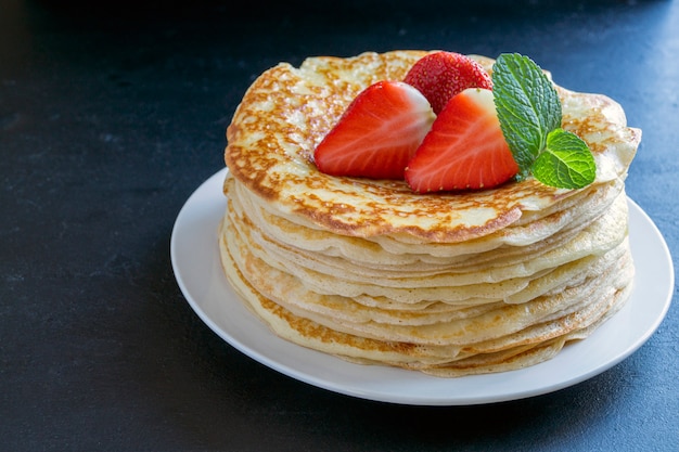 Pancakes with strawberries and mint on black background.