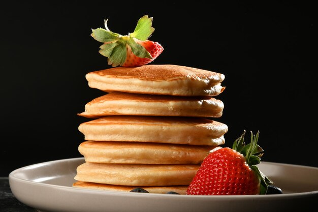 pancakes with sugar, strawberries and blueberries over dark texture.