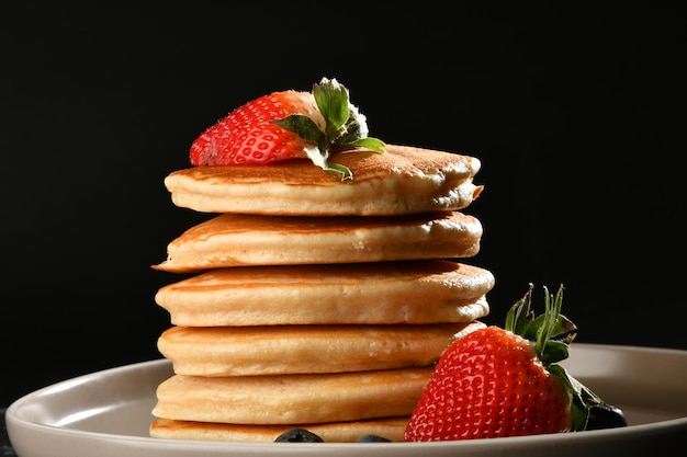 pancakes with sugar, strawberries and blueberries over dark texture.