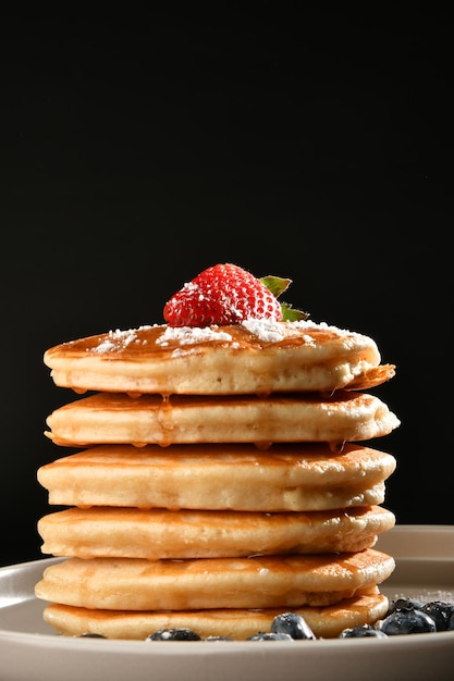 pancakes with sugar, strawberries and blueberries over dark texture.