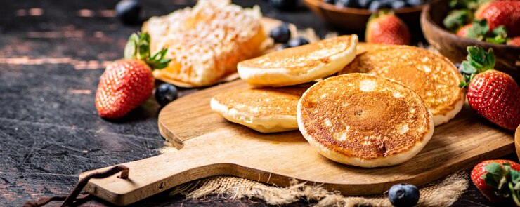 蜂蜜とベリーと木製のまな板上のパンケーキ