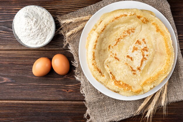 Pancakes on wooden table with ingredients beside