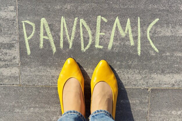 Pandemic concept, top view on woman legs and text written in chalk on gray sidewalk.