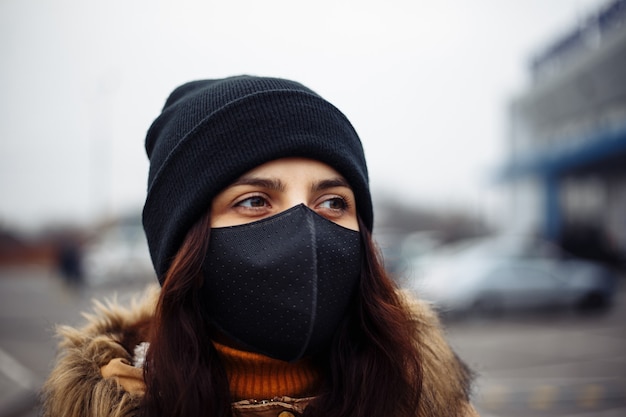 Пандемия коронавируса Молодая девушка на городской улице в черной маске для защиты от nCov 2019. Крупным планом - молодая женщина с хирургической стерильной маской. Карантин COVID-19 и концепция здоровья.