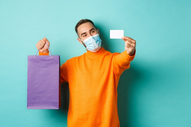 pandemic and lifestyle. Happy male customer in face mask showing credit card