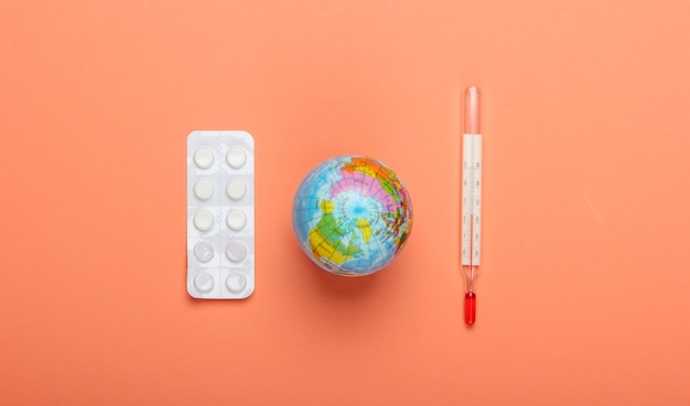 Pandemic outbreak or global warming concept. Globe, thermometer and blister of pills on orange  background. Top view