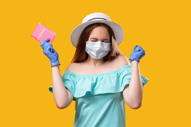 Pandemic tourism Global immigration Excited woman in protective face mask gloves with passport happy to get visa isolated on orange empty space Coronavirus quarantine restriction