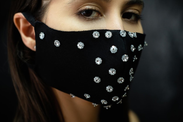 Pandemie mode DIY accessoire Quarantaine feestelijke look Close-up portret van mysterieuze vrouw in zwarte glamour herbruikbare handgemaakte stoffen gezichtsmasker met strass decor op donkere achtergrond