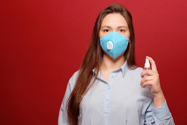 Pandemie van het coronavirus, close-upportret van jonge vrouw op rode achtergrond in beschermend medisch masker bespuit antiseptisch