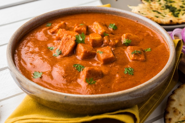 Paneer Butter Masala or Cheese Cottage Curry, popular Indian Lunch and Dinner menu  served in Karahi with Naan Or Roti over moody background, selective focus