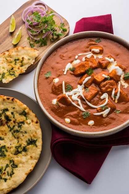 Paneer Butter Masala or Cheese Cottage Curry, popular Indian Lunch and Dinner menu  served in Karahi with Naan Or Roti over moody background, selective focus