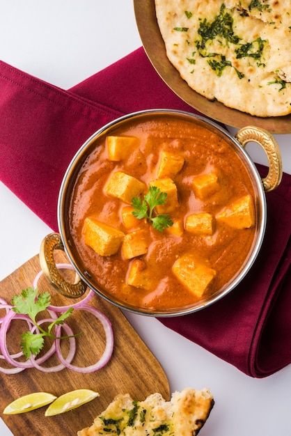 Paneer Butter Masala or Cheese Cottage Curry, popular Indian Lunch and Dinner menu  served in Karahi with Naan Or Roti over moody background, selective focus