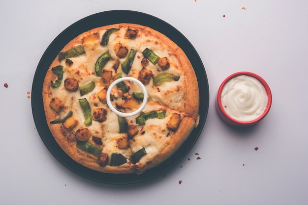 Paneer Pizza는 인도식 이탈리아 요리로 코티지 치즈를 얹고 화이트 소스를 곁들인 접시에 제공됩니다. 선택적 초점